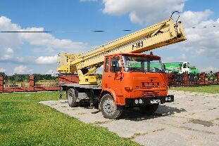 Pomarańczowy samochód ciężarowy Star z żółtym podnośnikiem koszowym na betonowym placu, widoczny numer F-163 na koszu, w tle ogrodzenie i zieleń.