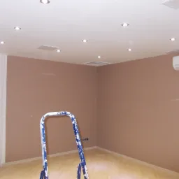 Pokój po odświeżeniu ścian w odcieniach brązu, widoczna drabina malarska z resztkami farby, oświetlenie sufitowe punktowe i klimatyzator na ścianie.