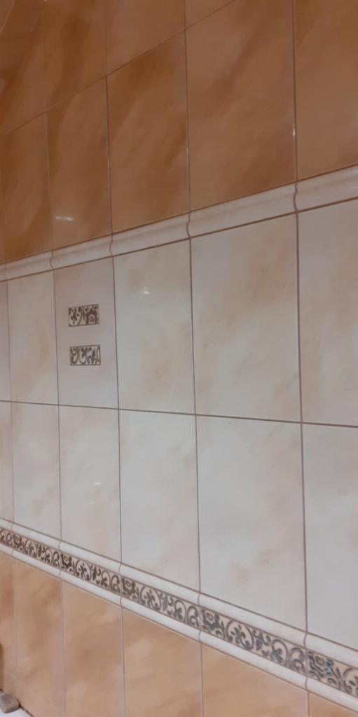 Wykończona ściana z beżowych płytek ceramicznych z dekoracyjnymi bordiurami i wstawkami z motywem ornamentów.