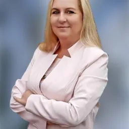 Portret kobiety w różowym żakiecie z założonymi rękami na rozmytym, gradientowym tle.