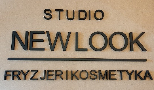Ściana z czarnym napisem 'STUDIO NEWLOOK FRYZJER I KOSMETYKA' wykonanym z grubych liter 3D.