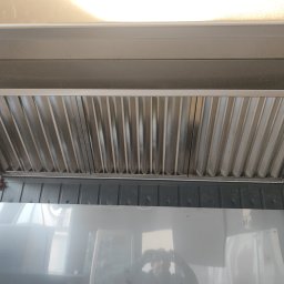 DD VENT - Wnętrze kanału wentylacyjnego z widocznym filtrem lamelkowym, zamontowanego pod sufitem, z odbiciem osoby robiącej zdjęcie na dolnej, błyszczącej powierzchni.