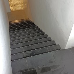 Artur Wolski usługi remontowo budowlane - Schody wyłożone ciemnymi, błyszczącymi płytkami ceramicznymi, widoczne ślady po fugowaniu, ściany pomalowane na biało.