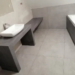 Nowoczesna łazienka w szarościach: umywalka nablatowa, obudowana wanna i płytki podłogowe. Minimalistyczny design, surowy betonowy styl wykończenia.