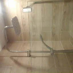 Nowoczesny zestaw prysznicowy z deszczownicą zamontowany na ścianie wyłożonej płytkami imitującymi drewno, widoczny w gotowej łazience.