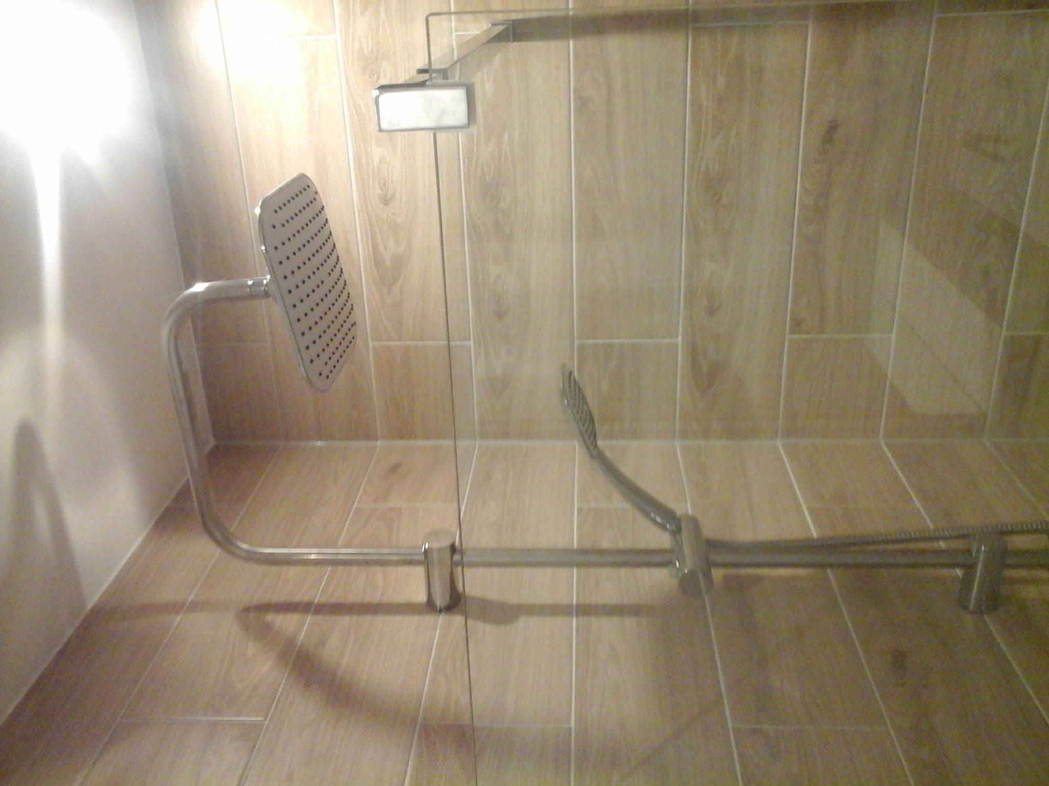 Nowoczesny zestaw prysznicowy z deszczownicą zamontowany na ścianie wyłożonej płytkami imitującymi drewno, widoczny w gotowej łazience.