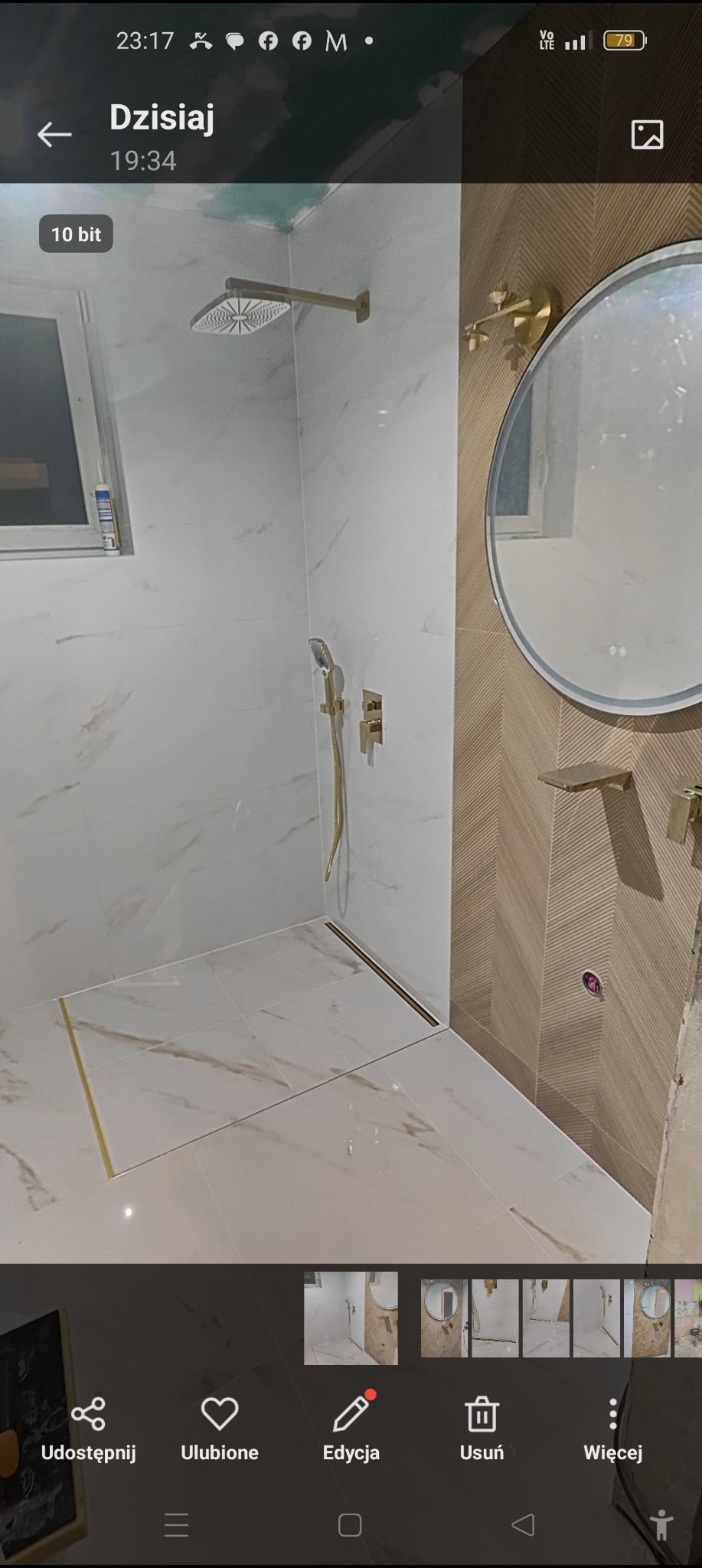 Nowoczesna kabina prysznicowa walk-in z białymi płytkami imitującymi marmur, złotą armaturą i odpływem liniowym, oraz ścianą z płytek ułożonych w jodełkę w odcieniach beżu.