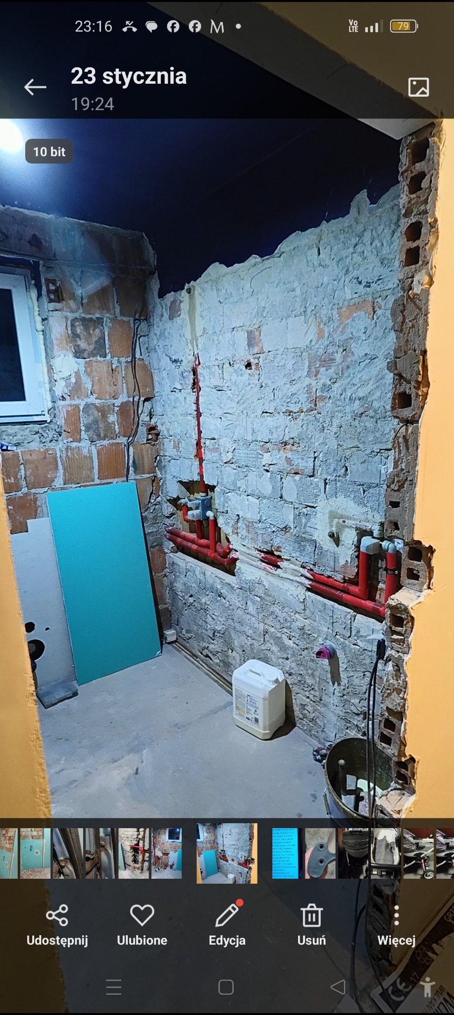 Remont łazienki w trakcie: odsłonięta cegła, nowe rury wodne w kolorze czerwonym, płyta gipsowa oparta o ścianę, widoczne przewody elektryczne.