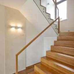 Nowoczesne drewniane schody z przeszkloną balustradą i oświetleniem ściennym, widok z dołu.