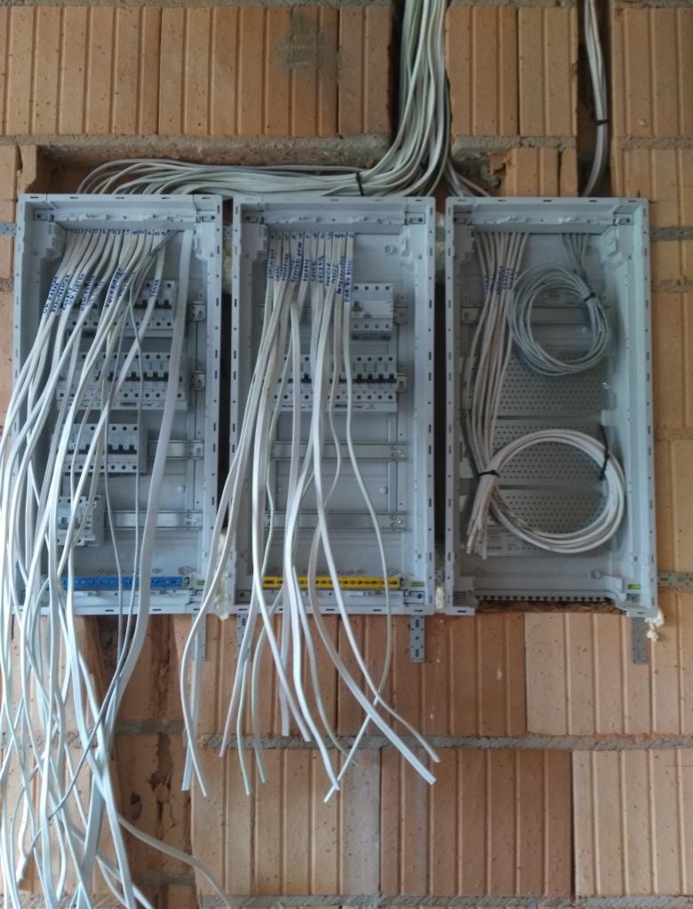 Trzy puste skrzynki rozdzielcze zamontowane na ceglanej ścianie z częściowo podłączonymi i oznaczonymi przewodami, w trakcie instalacji.
