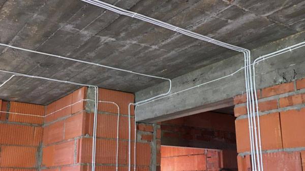 Białe rurki instalacyjne prowadzone po surowym, betonowym suficie i czerwonej, ceglanej ścianie w nowo budowanym pomieszczeniu.