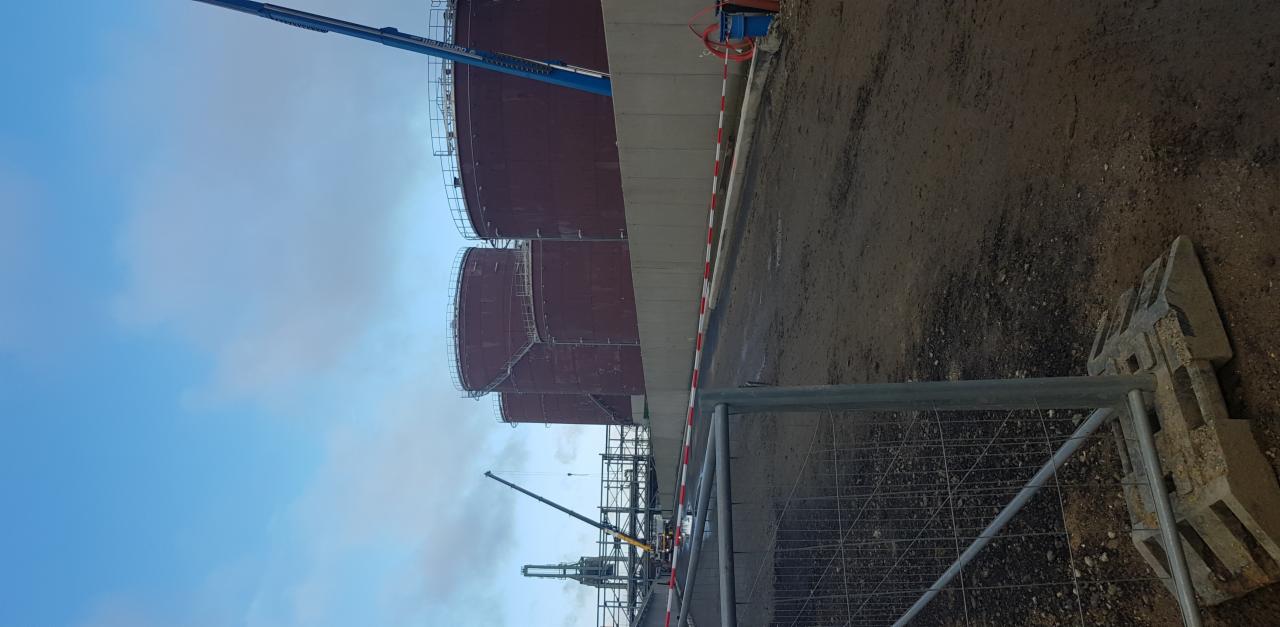 Montaż zbiorników przemysłowych w Żninie, widok z dołu na konstrukcje stalowe i podnośnik koszowy na tle pochmurnego nieba.