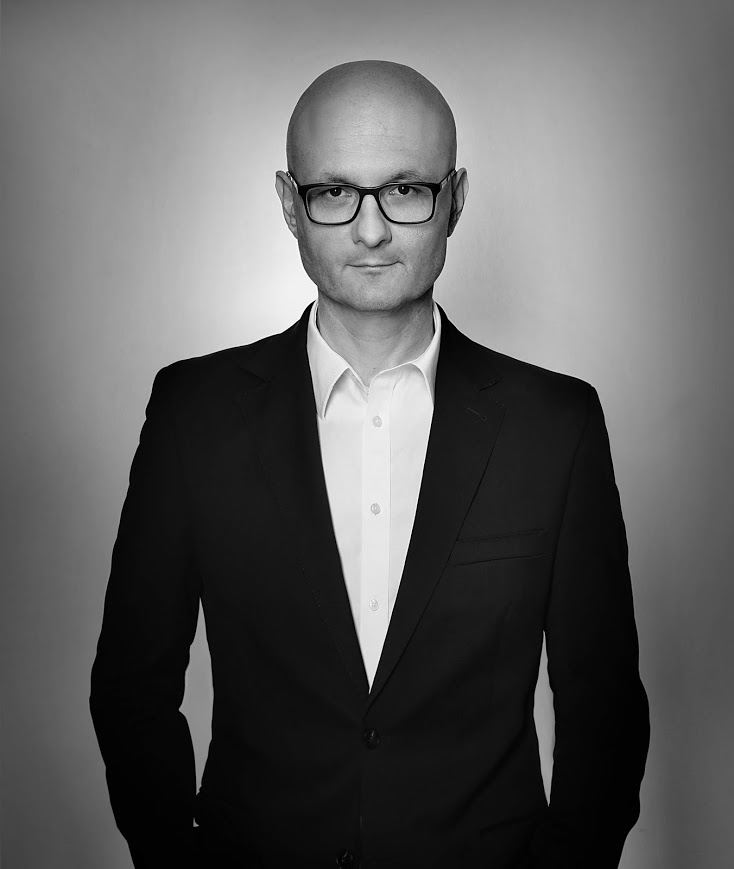 Portret biznesowy mężczyzny w okularach i czarnym garniturze na szarym tle, czarno-biały.