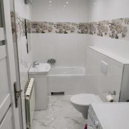 Cristal-Bud - Jasna łazienka z marmurową podłogą, wzorzystymi płytkami na ścianach, białą wanną, umywalką, toaletą i pralką, widziana z perspektywy drzwi.