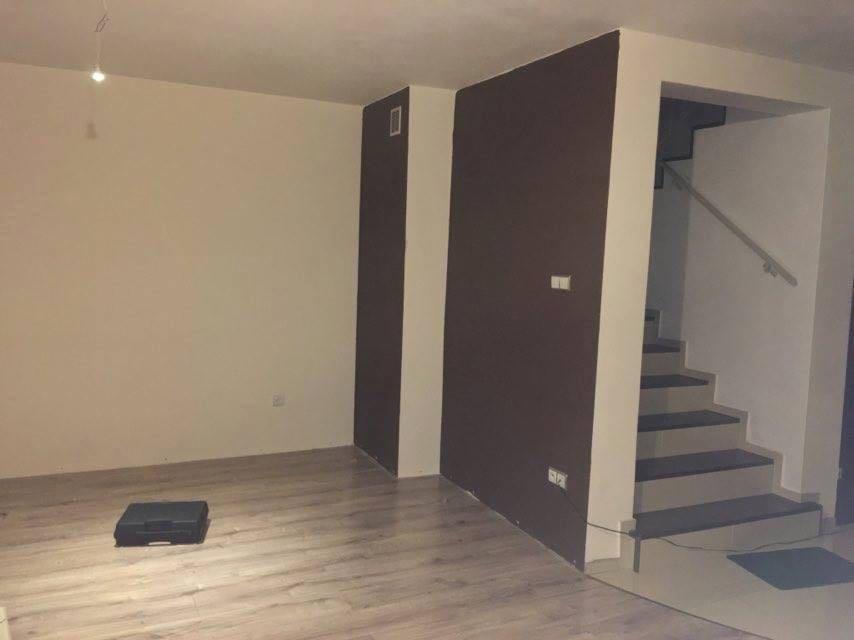 Pomalowane ściany w odcieniach beżu i brązu w pustym pokoju z drewnianą podłogą i schodami, widoczna skrzynka narzędziowa.