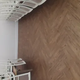 Ułożony parkiet w jodełkę francuską, widok z góry, fragment białego krzesła z kwiatami w lewym dolnym rogu.