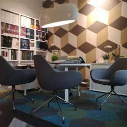 Wnętrze biura z nowoczesnymi fotelami na tle geometrycznej ściany i regału z próbkami materiałów, na podłodze wzorzysta, heksagonalna podłoga.