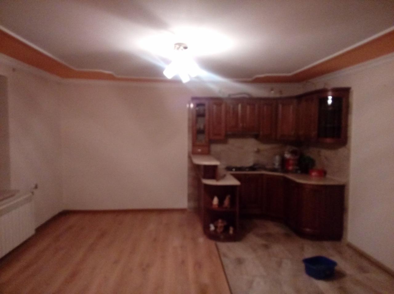 Częściowo wyremontowane wnętrze mieszkania z drewnianą zabudową kuchenną, panelami podłogowymi i fragmentem płytek, widoczne niedoskonałości wykończenia.