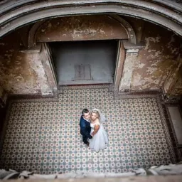 Para młoda w objęciach, sfotografowana z g&oacute;ry w okrągłym atrium z dekoracyjną, wzorzystą podłogą i łuszczącymi się ścianami.