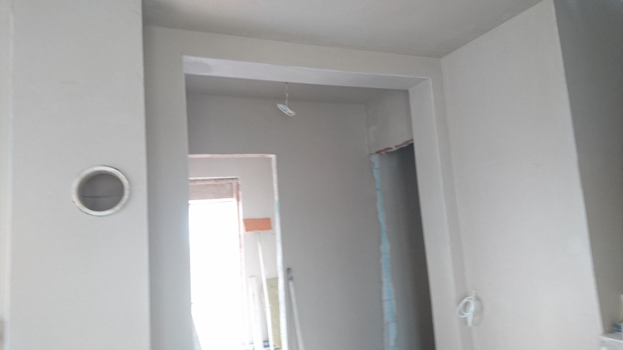 Świeżo wykończone, jasnoszare ściany w nowym mieszkaniu, widoczne otwory drzwiowe i instalacja elektryczna sufitowa, przygotowane do dalszych prac wykończeniowych.