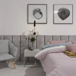 Nowoczesna sypialnia z łóżkiem w pastelowych odcieniach, szarym tapicerowanym zagłówkiem, minimalistycznymi grafikami na ścianie, lampką nocną i fotelem z drewnianymi nogami.
