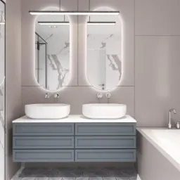 Nowoczesna łazienka z dwoma umywalkami nablatowymi, szarą szafką z szufladami, podświetlanymi owalnymi lustrami i wanną, wykończona panelami i płytkami imitującymi biały marmur z szarymi żyłami.