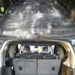 Bagażnik samochodu SUV przed czyszczeniem, widoczne zabrudzenia na gumowej macie i tapicerce, perspektywa od tylnej klapy.