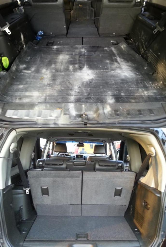 Bagażnik samochodu SUV przed czyszczeniem, widoczne zabrudzenia na gumowej macie i tapicerce, perspektywa od tylnej klapy.