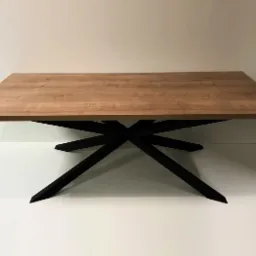 Prostokątny stół z blatem w kolorze jasnego drewna i czarną, geometryczną podstawą w kształcie gwiazdy.