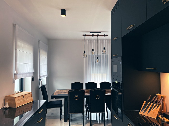 Nowoczesna kuchnia z czarnymi szafkami z frezowanymi uchwytami, marmurowym blatem stołu jadalnego i lampami wiszącymi w stylu industrialnym.