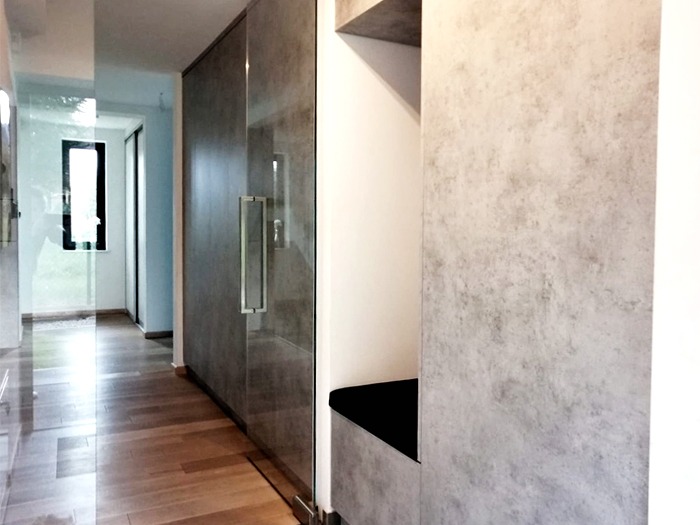 Nowoczesny korytarz z przesuwną szklaną szafą z szarymi panelami i drewnianą podłogą, widok z perspektywy wnętrza.