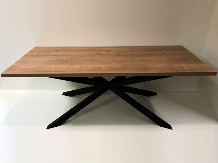 Prostokątny stół z blatem w kolorze jasnego drewna i czarną, geometryczną podstawą w kształcie gwiazdy.