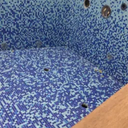 Wyłożona mozaiką w odcieniach błękitu niecka basenowa z przygotowanymi otworami na dysze, widoczna z perspektywy górnej w trakcie prac wykończeniowych we Wrocławiu.