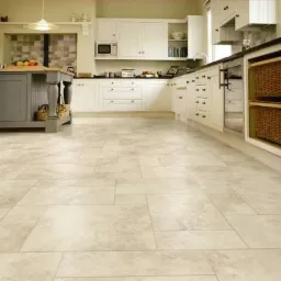 Jasna, przestronna kuchnia z beżową podłogą z płytek imitujących kamień, białe szafki z ciemnym blatem, wyspa kuchenna w kolorze szarym i wiklinowe kosze.