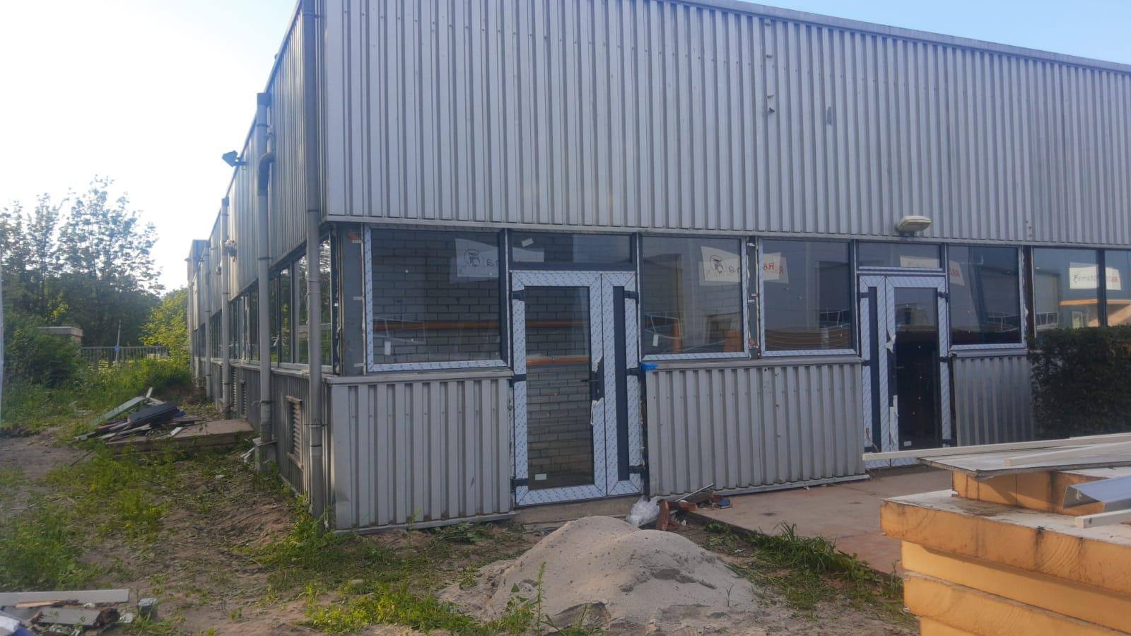 Budynek z blachy falistej z zamontowanymi oknami i drzwiami z białymi ramami, widoczne ślady po montażu i pozostałości materiałów budowlanych na zewnątrz.