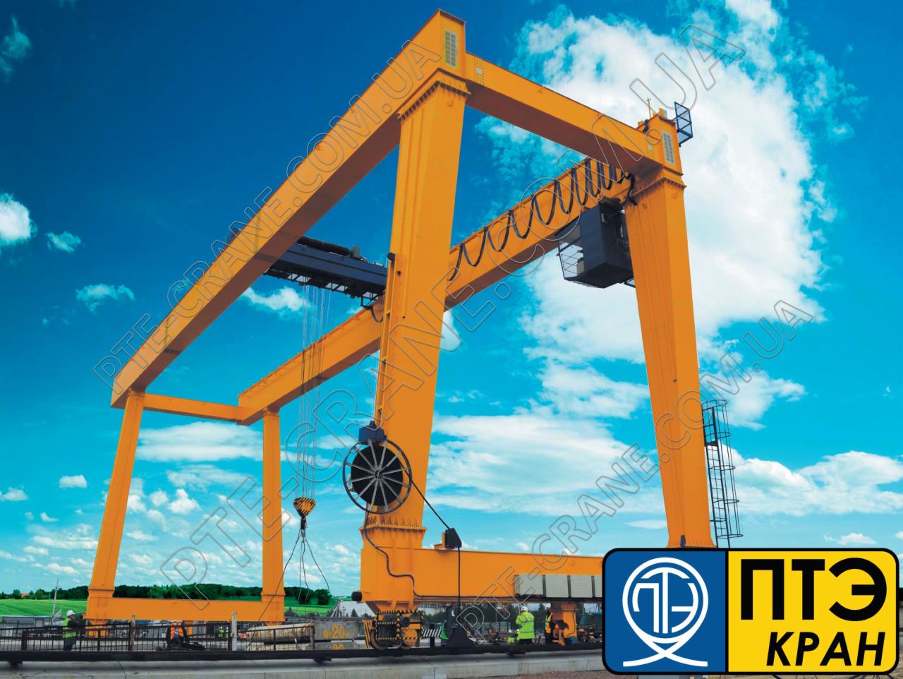 Żółty suwnicowy dźwig bramowy z podwieszonym ładunkiem na tle błękitnego nieba z chmurami, z widocznym logo producenta w prawym dolnym rogu.