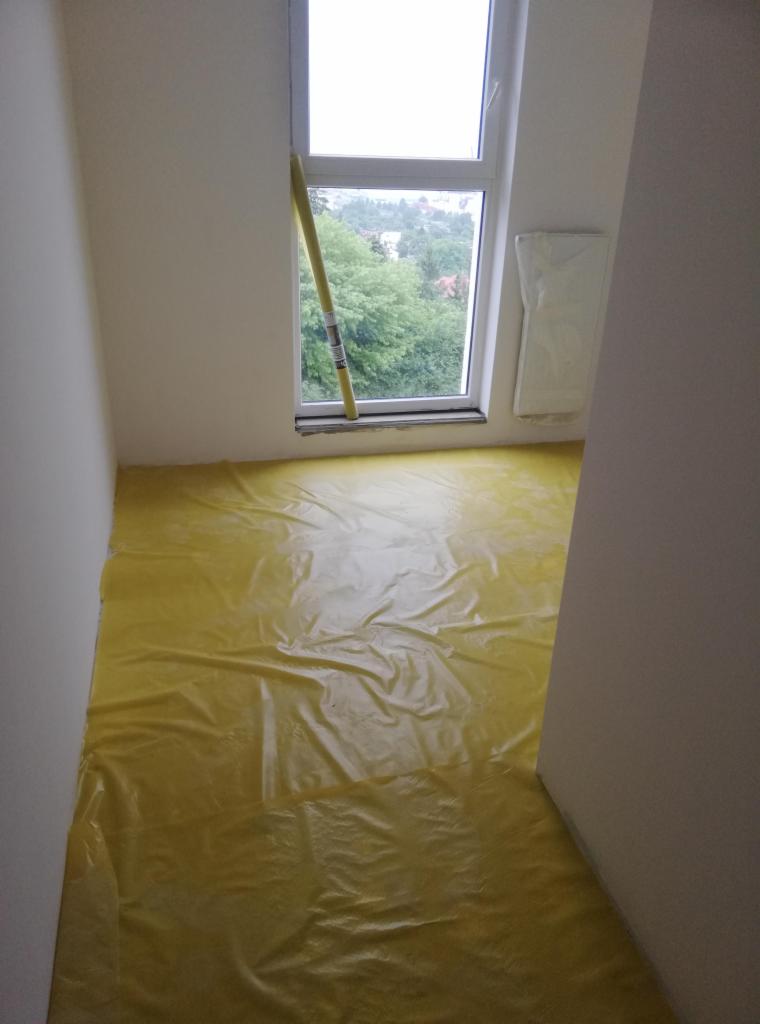Pokój zabezpieczony żółtą folią malarską przed rozpoczęciem prac, widoczny zwinięty wałek malarski oparty o okno.