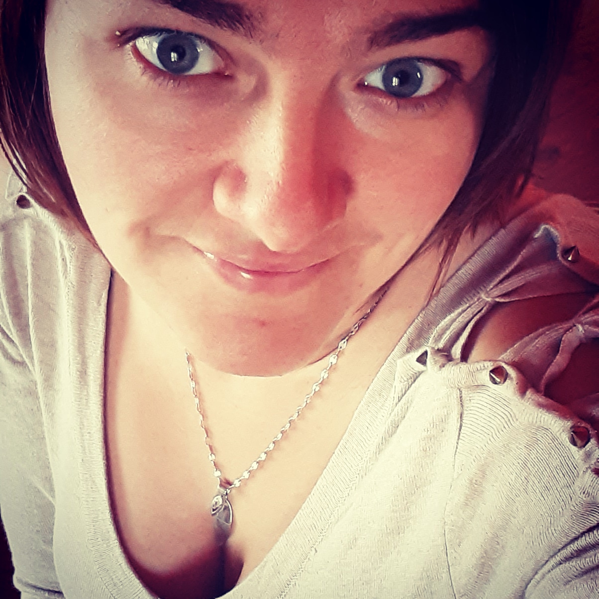 Portret kobiety z kolczykiem w brwi, w szarej bluzce z ozdobnymi nitami i srebrnym naszyjnikiem, z bliska, z góry.