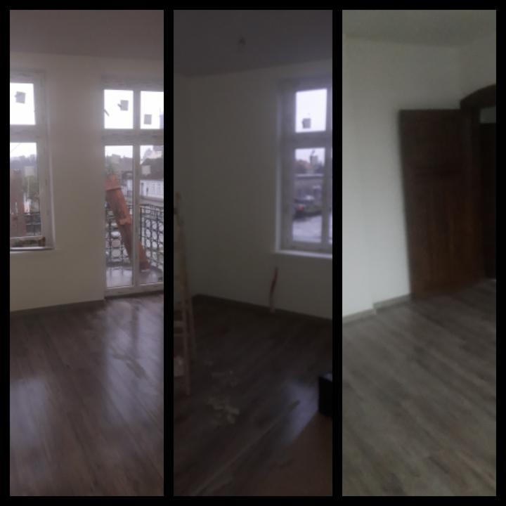 Wnętrze pokoju po odświeżeniu ścian, widoczne okna z naklejoną folią ochronną i ciemna podłoga z drobnymi zabrudzeniami.