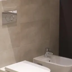 Nowoczesna łazienka z beżowymi płytkami, wiszącą miską WC i bidetem z chromowaną armaturą.