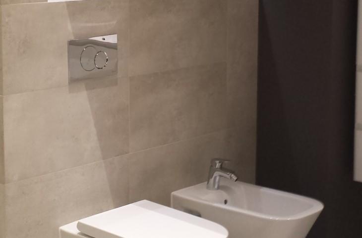 Nowoczesna łazienka z beżowymi płytkami, wiszącą miską WC i bidetem z chromowaną armaturą.