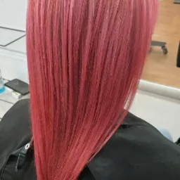 Tył głowy z włosami w odcieniach różu i czerwieni, świeżo po koloryzacji z widocznymi refleksami, na tle salonu z lustrami i sprzętem.