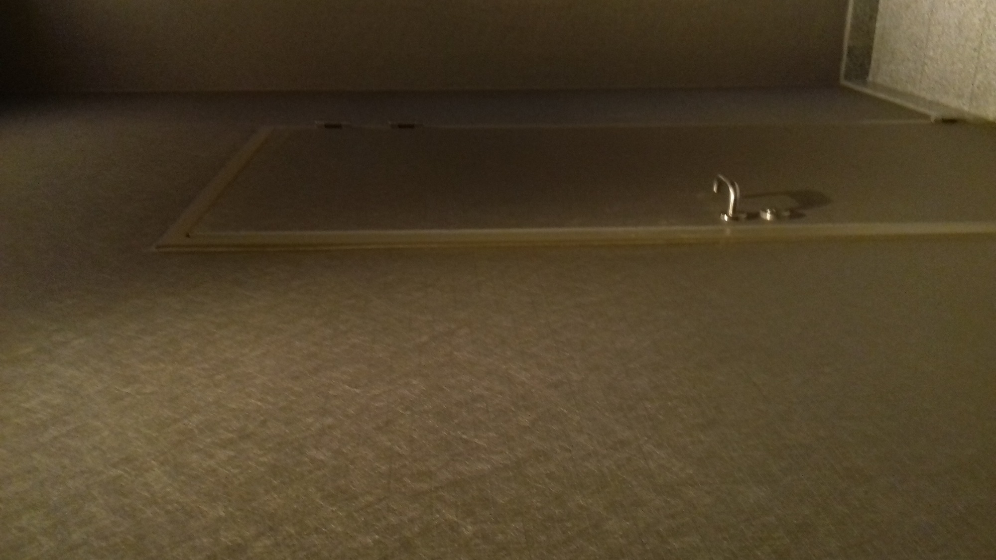 Szara tapeta na ścianie z widocznym włazem rewizyjnym z metalowym uchwytem.