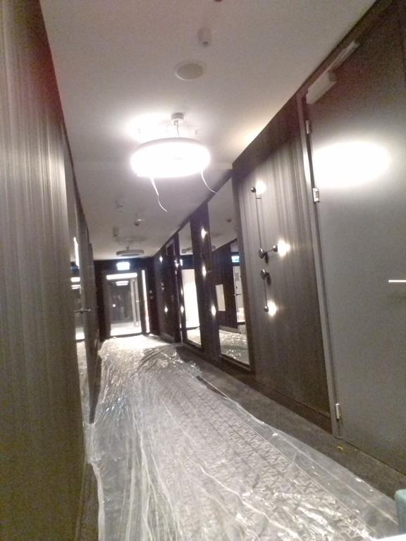 Korytarz w trakcie zabezpieczania folią przed pracami wykończeniowymi ścian z widocznymi drzwiami i oświetleniem sufitowym.