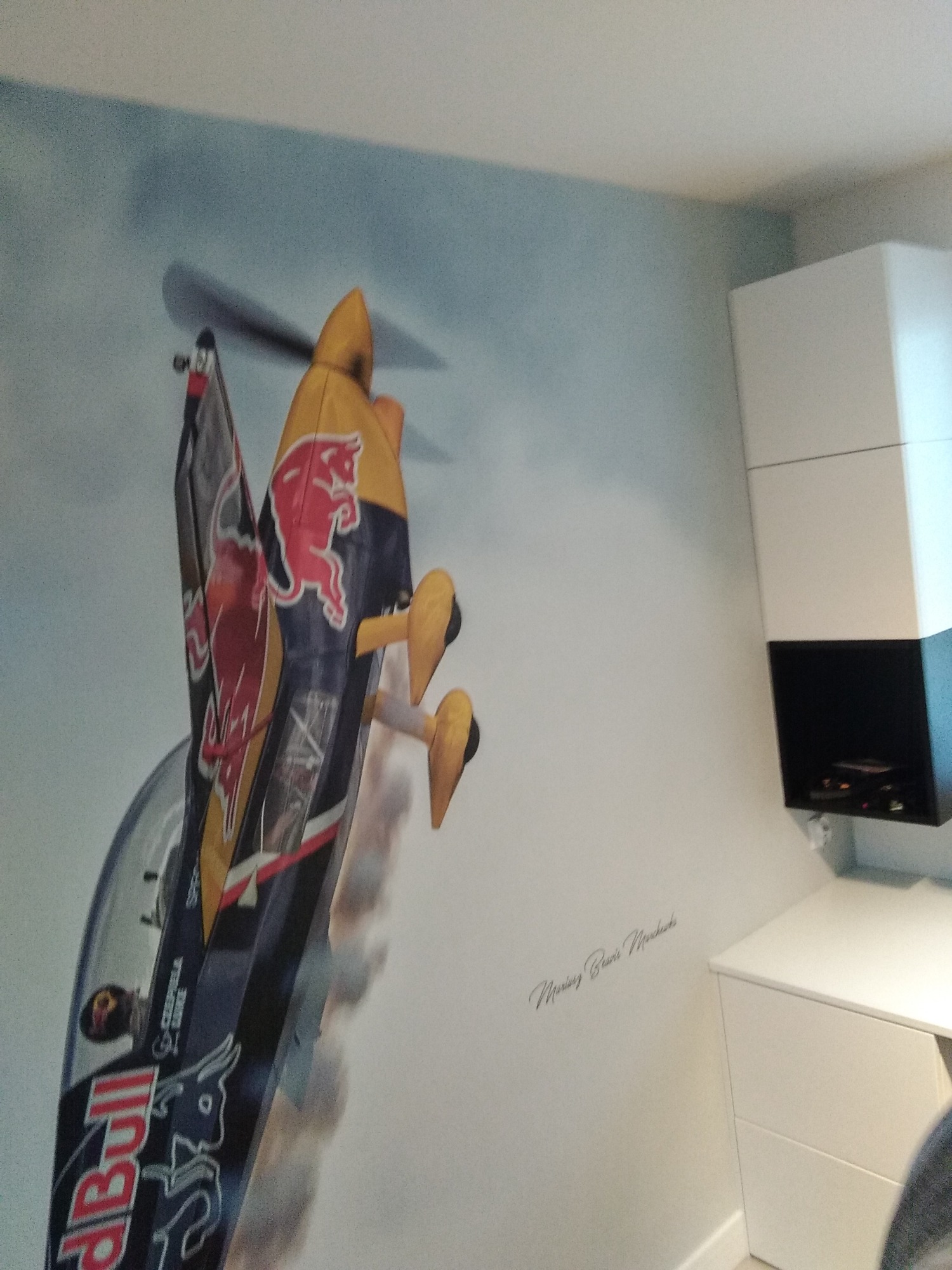 Ściana pokoju z fototapetą przedstawiającą samolot akrobacyjny Red Bull z widocznymi detalami konstrukcji i logotypami, obok białe meble.