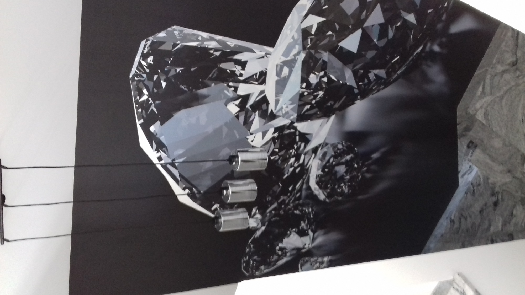 Fototapeta z motywem dużych, fasetowanych kryształów w odcieniach szarości, zamocowana na ścianie za pomocą metalowych uchwytów szynowych.