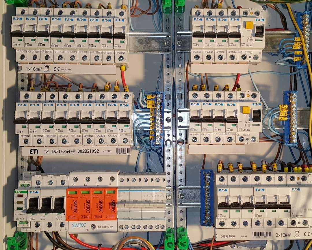 Rozdzielnica elektryczna z zabezpieczeniami nadprądowymi i różnicowoprądowymi, widoczne przewody, szyny DIN i oznaczenia EATON oraz SIMTEC. Instalacja starannie wykonana, widoczne etykiety...