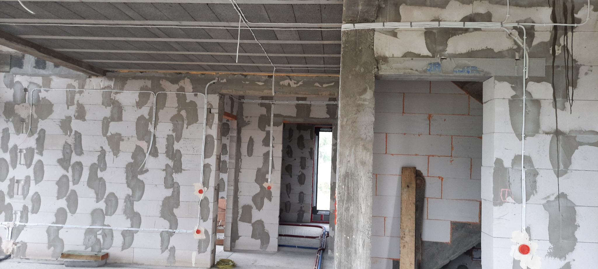 Wnętrze surowego budynku w trakcie prac, widoczne rozprowadzone przewody elektryczne w białych peszlach, puszki pod gniazdka i włączniki, ściany z betonu komórkowego z widocznymi śladami zaprawy.