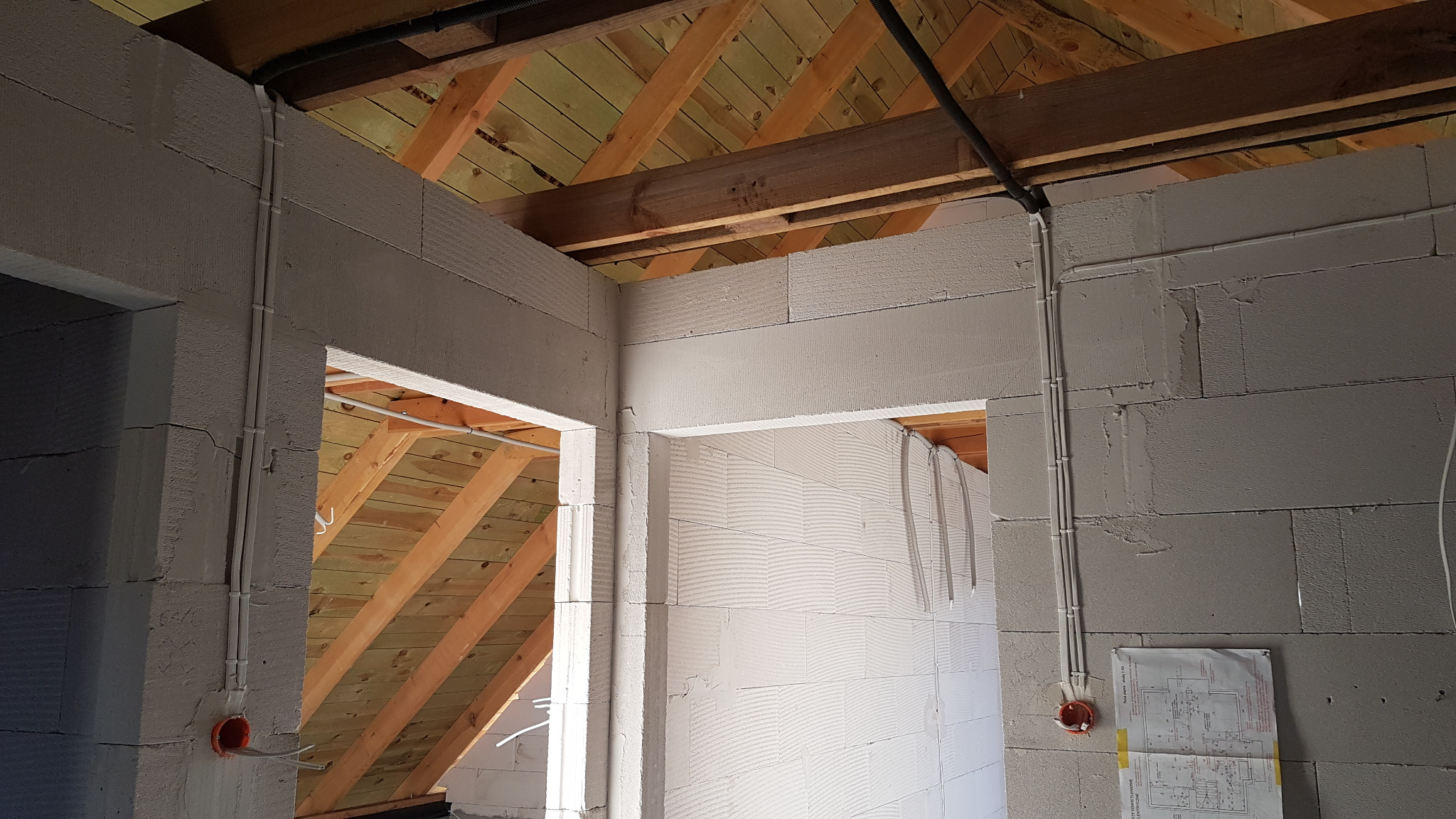 Wewnętrzne instalacje elektryczne prowadzone po ścianach z betonu komórkowego, widoczne rury instalacyjne, puszka elektryczna i fragment planu instalacji.