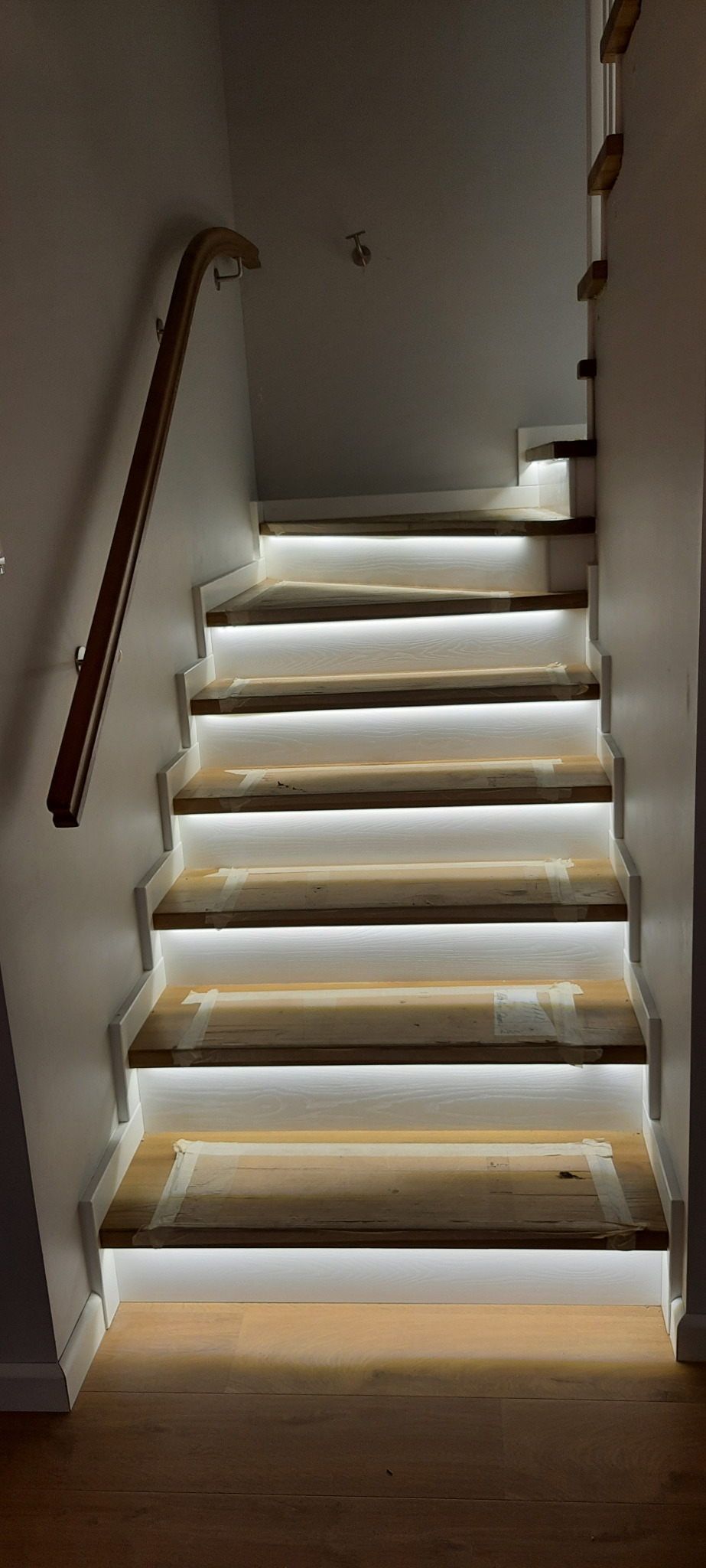 Schody drewniane z podświetleniem LED, zabezpieczone taśmą malarską podczas montażu, widoczna drewniana poręcz.